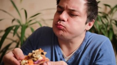Büyük bir zevkle güzel bir adam mantarlı, domatesli, biberli ve peynirli vejetaryen pizza yer. Pizza dilimlerini düşürür ve toplar. Genç bir adam bir dilim pizza tutuyor, bir ısırık alıyor ve çiğniyor. Yakın plan..