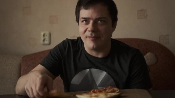 黒Tシャツの男がおいしいピザを食べています 若い男は ピザのスライスを取り 一口を取り それを噛む — ストック動画