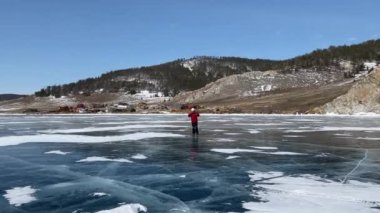 Baykal Gölü 'nde buz pateni. Kırmızı ceketli, beyaz kasklı, patenli ve kayak sopalı bir adam donmuş Baykal Gölü 'nün buzunda kayıyor. Temiz, pürüzsüz mavi şeffaf buz ve derin çatlaklarla güzel bir kış manzarası. Olkhon Adası.
