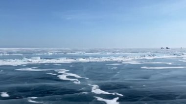 Donmuş Baykal Gölü 'nün Panorama' sı. Uzakta bir grup turist paten geziyor. Mavi şeffaf buzla kaplı güzel bir kış manzarası derin çatlaklar, küçük hummozlar ve kar adaları.