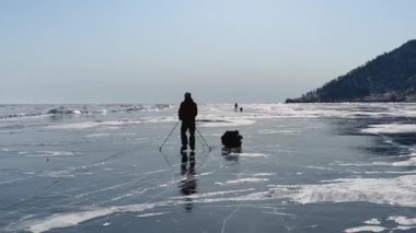 Buz pateni yapan iki turist, buz tutmuş Baykal Gölü 'nün buzunda kayak sopaları ve sürükleme aletleriyle geziyorlar. Temiz, pürüzsüz mavi şeffaf buz ve derin çatlaklarla güzel bir kış manzarası..