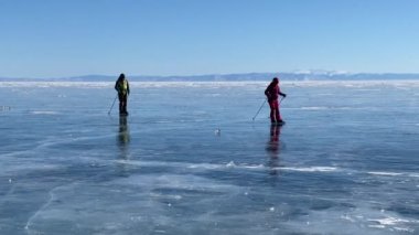 Baykal Gölü 'nde buz pateni. Bir adam ve bir kız buz tutmuş Baykal Gölü 'nün buzunda kayak sopalarıyla kayıyorlar. Temiz, pürüzsüz mavi şeffaf buz ve derin çatlaklarla güzel bir kış manzarası..