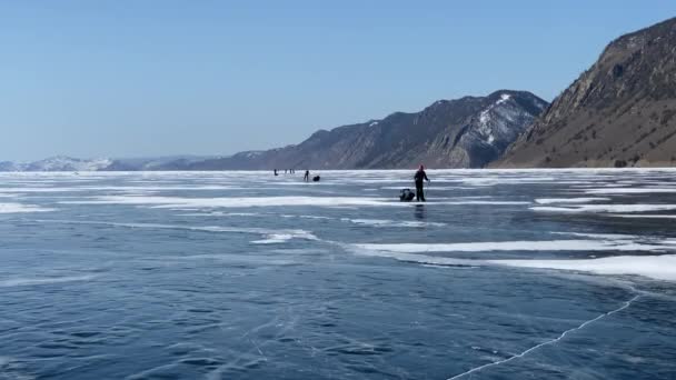 凍結したバイカル湖の氷の上のアイススケートを旅行する観光客のグループ 深い亀裂や雪の島と青透明な氷と美しい冬の風景 オルホン島 — ストック動画