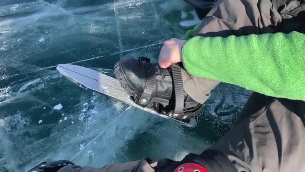 一个穿着绿色毛衣 橙色头盔和红色膝盖垫的家伙穿上冰鞋在冰上滑冰 滑板上有特写 白加尔湖结冰 冰面光滑透明 裂缝很深 — 图库视频影像
