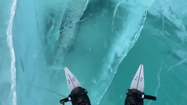 男が凍ったバイカル湖でスケートをしている 脚の上からの眺め 接近中だ 深い亀裂と青透明な透明な滑らかな氷 ロシアの自然ランドマーク — ストック動画