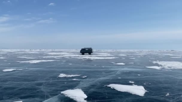 人们乘坐一辆苏联汽车在冰冻的贝加尔湖冰上旅行 透明的蓝冰 有深深独特的裂缝和积雪漂移在蓝天之上 美丽的冬季风景 — 图库视频影像