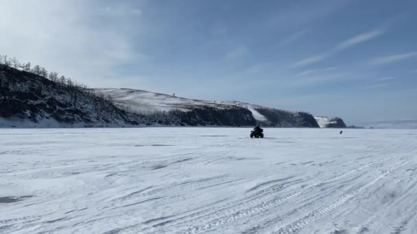 那家伙在白加尔湖冰封的雪地上骑越野车贝加尔湖的冬季活动 奥尔康岛 有小山 小山和珍贵的树木 — 图库视频影像