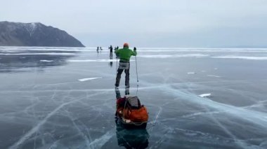 Baykal Gölü 'nde buz pateni. Sürüklenen ve patenli bir grup turist donmuş Baykal Gölü boyunca seyahat ediyor. Derin çatlakları ve kar adaları olan şeffaf mavi buzla güzel bir kış manzarası. Olkhon Adası.