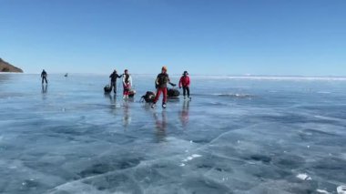 BAIKAL, IRKUTSK REGION, RUSSIA - 18 Mart 2021: Bir grup turist donmuş Baykal Gölü buzu üzerinde paten ile seyahat ediyor. Derin çatlakları olan saydam mavi buzla güzel bir kış manzarası..