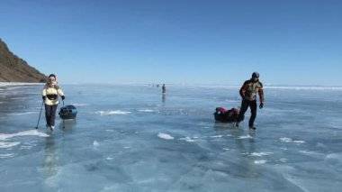 BAIKAL, IRKUTSK REGION, RUSSIA - 18 Mart 2021: Bir grup turist donmuş Baykal Gölü buzu üzerinde paten ile seyahat ediyor. Derin çatlakları olan saydam mavi buzla güzel bir kış manzarası..