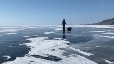 BAIKAL, IRKUTSK REGION, RUSSIA - 17 Mart 2021: Güzel bir kız donmuş Baykal Gölü 'nün buzunda paten üzerinde seyahat eder. Derin çatlakları olan mavi şeffaf buz.