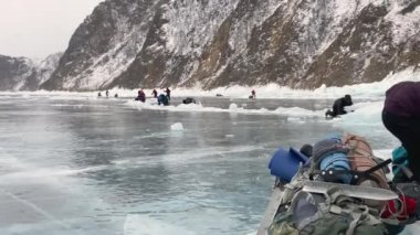 BAIKAL, IRKUTSK REGION, RUSSIA - 16 Mart 2021: donmuş Baykal Gölü üzerinde şiddetli rüzgar. Turistler mavi şeffaf buz üzerinde derin çatlaklar olan bir kasırga tarafından uçurulurlar. Kış yürüyüşü.
