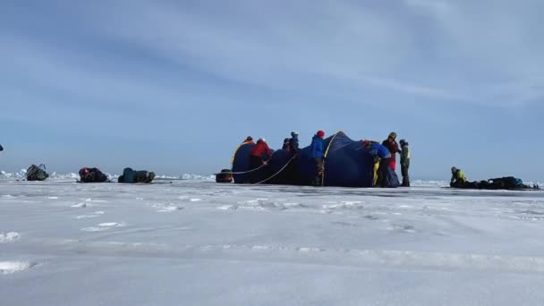 バイカル イルクーツク地方 ロシア 2021年3月16日 凍結したバイカル湖の氷の上に2つの冬のテントを設置する観光客のグループとしてのタイムラプス 深い亀裂と青透明な氷 冬のハイキング — ストック動画