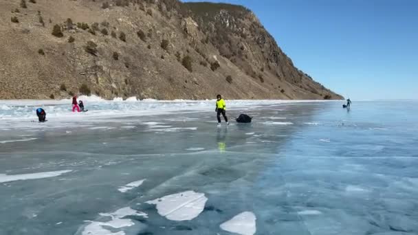 バイカル イルクーツク地域 ロシア 2021年3月18日 観光客は凍結したバイカル湖の氷の上のスケートで旅行します 深い亀裂の青い透明な氷と美しい冬の風景 — ストック動画