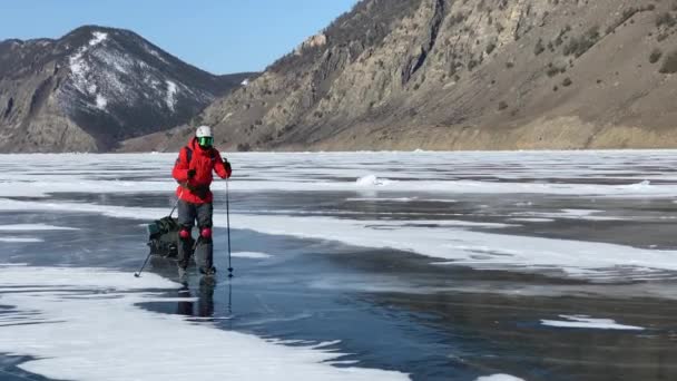 Baikal Irkutsk Region Russia 2021年3月17日 オレンジのジャケット ヘルメット サンマスクの男が深い亀裂の青い透明な氷で凍結したバイカル湖の氷の上でスケートしている — ストック動画