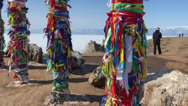 ロシア イルクーツク州オルコン島 2021年3月15日 ブルクハン岬シャマンカ近くの聖地へのリボンを結ぶ女性 カラフルなチベット仏教のリボン極風になびくタイ — ストック動画