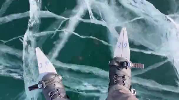在冰冻的贝加尔湖上 一个男人正在滑冰 戴着红色的膝垫 腿的上视图 蓝色透明透明的光滑冰 有深深的裂缝 俄罗斯的自然地标 — 图库视频影像