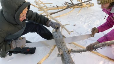 İki kız iki elle testereyle odun kesiyor. Turistler yakacak odun hazırlıyorlar. Kuzey manzarası. Kış yürüyüşü. Olkhon Adası, Rusya 'nın doğal bir simgesi..