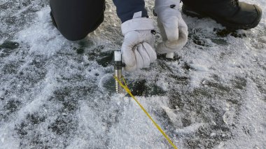 Beyaz eldivenli bir kız çadırın kemerlerini çizmek için buz vidasını buza sokuyor. Elleri yakın çekim. Donmuş Baykal Gölü. Kış yürüyüşü.