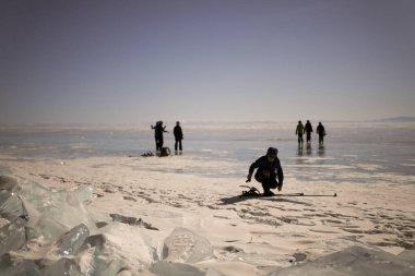 Turistler donmuş Baykal Gölü boyunca seyahat ederler. Derin çatlakları ve kar adaları olan şeffaf mavi buzla güzel bir kış manzarası. Olkhon Adası.