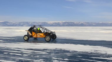 BAIKAL, IRKUTSK REGION / RUSSIA - 11 Mart 2021: Bir adam donmuş gölde turuncu bir rali arabası kullanıyor. Baykal Gölü 'nde turistler için eğlence. Mavi buzlu güzel kış manzarası.