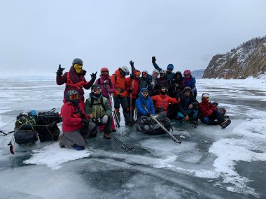 BAIKAL, IRKUTSK REGION / RUSSIA - 18 Mart 2021: Bir grup turist donmuş Baykal Gölü 'nün buzunda kask ve güneş maskesi takıyor. Derin çatlakları olan saydam mavi buzla güzel bir kış manzarası..