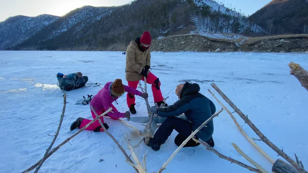 Three girls are preparing firewood. Tourists are sawing wood with a two-handed saw. Northern landscape. Winter hike. Olkhon Island, a natural landmark of Russia.