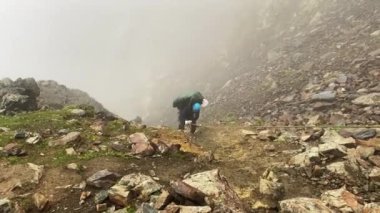 Mavi kasklı, büyük sırt çantalı bir dağcı yokuş yukarı tırmanır. Rusya 'nın kuzeyinden Kazbek' e tırmanıyor. Kafkasya 'yı yürüyerek geçmek. Yatay korkuluklar.