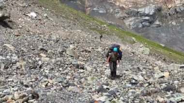 Mavi kasklı, büyük sırt çantalı bir adam taşların dağılması boyunca yokuş yukarı yürüyor. Rusya 'nın kuzeyinden Kazbek' e tırmanıyor. Kafkasya 'da yürüyüş.