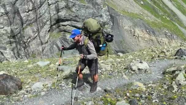 大きなバックパックを持つハイカーは山道を歩いています 北からカズベク登山 ロシアの側から コーカサスを横断するハイキング — ストック動画