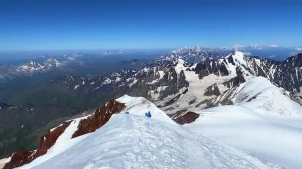 一人の登山家がカズベク山の頂上から降りてくる 岩や丘の壮大なパノラマ 北からカズベク登山 ロシアの側から コーカサスを横断するハイキング — ストック動画