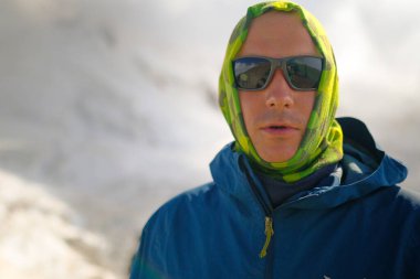 Yeşil tenli ve dağ gözlüklü bir adamın portresi. Turist dağcı beyaz bulutlarla mavi gökyüzüne bakar. Rusya 'nın kuzeyinden Kazbek' e tırmanıyor. Kafkasya 'da yürüyüş.