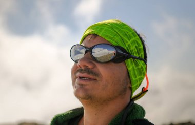 Dağ gözlüklü traşsız bir adamın portresi. Dağın arka planında bir turist tırmanışçısı. Rusya 'nın kuzeyinden Kazbek' e tırmanıyor. Kafkasya 'da yürüyüş.