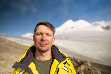 Dağlardaki yorgun ve ciddi bir adamın portresi. Kazbek Dağı 'nın arka planındaki turist tırmanışçısı. Rusya 'nın kuzeyinden Kazbek' e tırmanıyor. Kafkasya 'da yürüyüş.