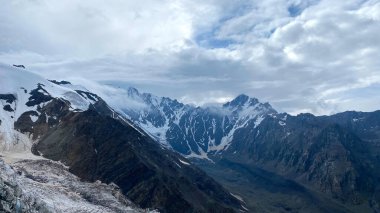 Karla kaplı dağlar, ulaşılamaz kayalar, mavi gökyüzü ve beyaz bulutlar. Kuzey Osetya 'nın dağ manzarası. Kuzeyden, Rusya 'dan gelen Kazbek tırmanışı. Kafkasya 'da yürüyüş.