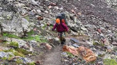 Turuncu kasklı, büyük sırt çantalı mutlu bir turist dağ yoluna çıkıyor. Rusya 'nın kuzeyinden Kazbek' e tırmanıyor. Kafkasya 'da yürüyüş.