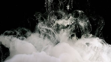 Suya beyaz mürekkep damlaları. Siyah arka planda beyaz mürekkep bulutu. Kozmik büyü soyut arka plan. Suyun içinde beyaz suluboya boya.