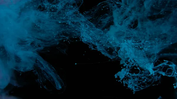 Drops of blue ink in water. Blue watercolor paints in water on a black background. Awesome abstract background. Beautiful wallpaper for your desktop. Blue cloud of ink on a black background.