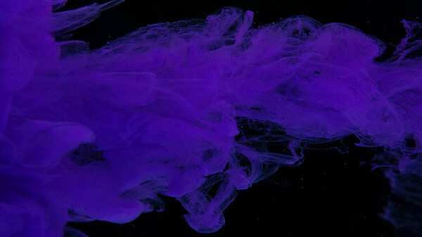 Drops of purple ink in water. Purple watercolor paints in water on a black background. Awesome abstract background. Beautiful wallpaper for your desktop. Violet cloud of ink on a black background.