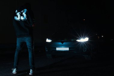 Genç adam gece boyunca arabasının önünde duruyor.