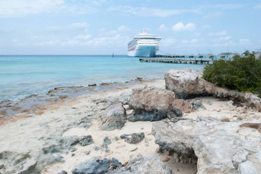 Arkaplanda kayalık bir Büyük Türk adası sahili ve demirlemiş bir yolcu gemisi (Turks ve Caicos Adaları) manzarası).