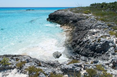 Half Moon Cay üzerinde kayalık sarp kıyı şeridi ve turkuaz renkli su üzerinde yaşam olmayan ada (Bahamalar)).