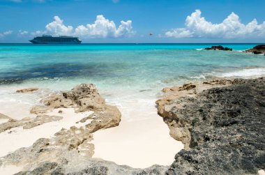 Half Moon Cay adasındaki kayalık sahil manzarası ve arka planda sürüklenen bir yolcu gemisi (Bahamalar). 