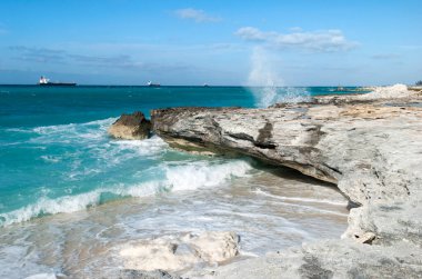 Büyük Bahama adasında dalgaların ve arka planda sanayi gemilerinin olduğu aşınmış bir kıyı şeridi manzarası.