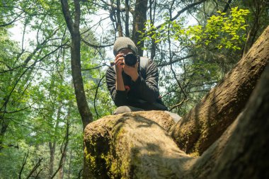 Ormanın içinde profesyonel bir kamerayla fotoğraf çeken bir adam.