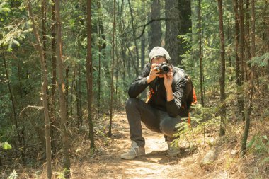 Ormanın içinde profesyonel bir kamerayla fotoğraf çeken bir adam.