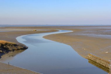 Hollanda, Zeeland 'deki Scheldt nehrinin çamurlu düzlüklerinde kışın mavi gökyüzü ile polderi sulamak için dönen büyük bir kanal.