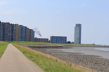 the skyline in terneuzen with flats and apartment buildings and the mudflats of the westerschelde sea along the boulevard in front in summer clipart