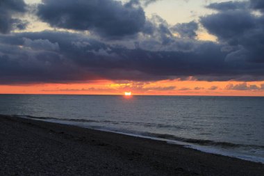 Normandiya 'da Fransız sahillerinde güzel bir gün batımı turuncu bir güneş ve denizin üstünde büyük gri bulutlar.
