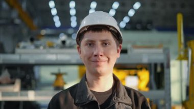 Kasklı tamirci dikkatle kameraya bakıyor. Birkaç saniye sonra gülümsemeye başlıyor..